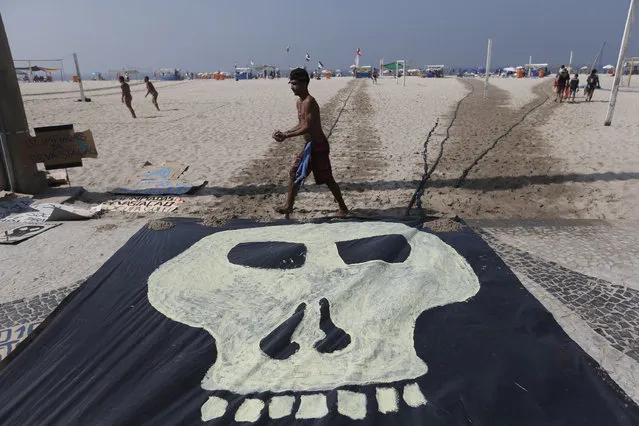 A man walks past a banner with a drawing of a skull symbolizing the death of nature during a protest on the Copacabana beach in Rio de Janeiro, Brazil, Saturday, August 1, 2015. Less than a dozen people showed up for a scheduled protest by environmentalists against the money spent in preparation for the Olympics and the construction of the game's golf course that was partially carved out of a nature reserve. (Photo by Silvia Izquierdo/AP Photo)