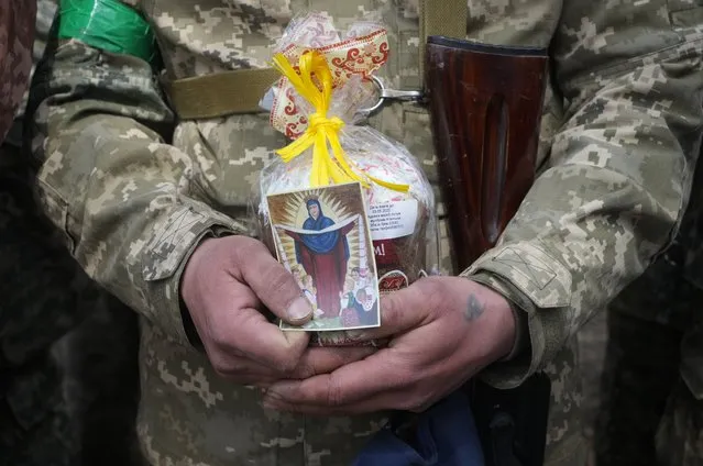 A Ukrainian soldier holds an Easter cake and an icon during a blessing ceremony on Easter eve at a military position outside Kyiv, Ukraine, Saturday, April 23, 2022. (Photo by Efrem Lukatsky/AP Photo)