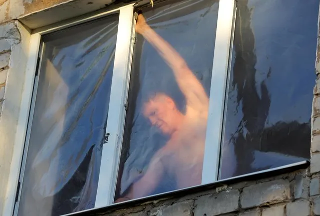 A local resident uses a plastic tape to cover a broken window in an apartment building located in Vannikova street following recent shelling in the course of Ukraine-Russia conflict in Donetsk, Ukraine on June 20, 2022. (Photo by Alexander Ermochenko/Reuters)