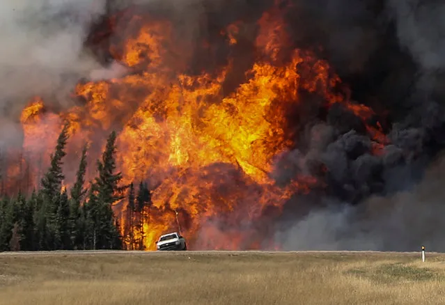 Smoke and flames from the wildfires erupt behind a car on the highway near Fort McMurray, Alberta, Canada, May 7, 2016. (Photo by Mark Blinch/Reuters)