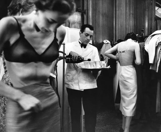 At a fashion show in France, John Cavanagh's models change backstage as a waiter pours champagne, 1953