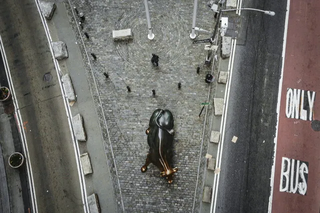 A lone pedestrian walks down Broadway past the Charging Bull statue as COVID-19 concerns empty a typically bustling downtown area, Saturday, March 21, 2020, in New York. New York Gov. Andrew Cuomo announced sweeping orders Friday that will severely restrict gatherings of any size for the state's more than 19 million residents and will require workers in nonessential businesses to stay home. (Photo by John Minchillo/AP Photo)