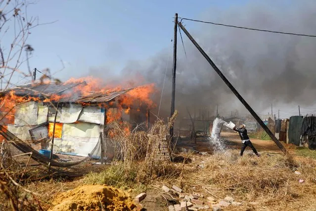 A resident attempts to extinguish a fire after a shack (informal housing structure) belonging to a man, who is suspected of helping illegal miners in the area, was set on fire while residents protest against illegal mining and rising crime in the area in Kagiso on August 4, 2022. (Photo by Guillem Sartorio/AFP Photo)