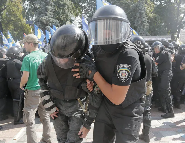 A police officers comes to the aid of his injured colleague  during a clash between protesters and police after vote to give greater powers to the east, outside the Parliament, Kiev, Ukraine, Monday, August 31, 2015. (Photo by Efrem Lukatsky/AP Photo)