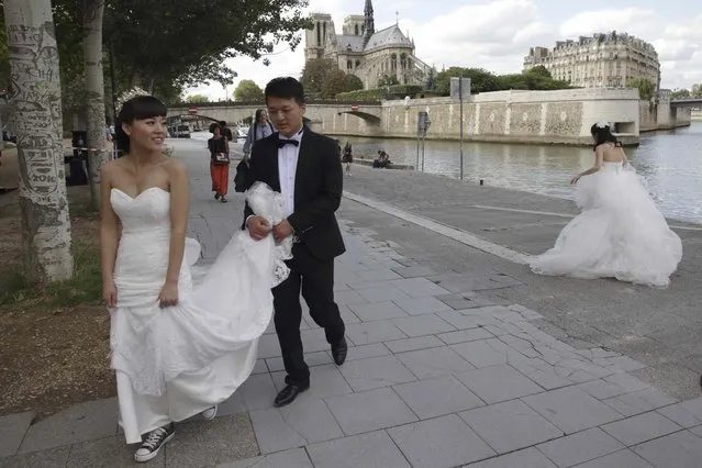 A Chinese couple walks near an other future bride during a pre-wedding photoshoots in front of the Notre-Dame Cathedral in Paris, France, August 28, 2015. (Photo by Philippe Wojazer/Reuters)