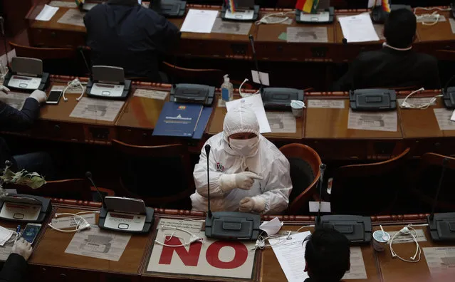 A lawmaker wearing protective gear attends a session at Congress' Plurinational Legislative Assembly in La Paz, Bolivia, Friday, April 17, 2020. Amid the spread of the new coronavirus, other lawmakers are attending sessions virtually. The sign “no” is used by politicians who are opposition to the government of former President Evo Morales. (Photo by Juan Karita/AP Photo)
