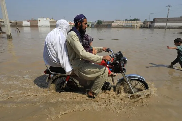 A family travels on a motorbike along a flooded road, following rains and floods during the monsoon season in Nowshera, Pakistan on August 30, 2022. (Photo by Fayaz Aziz/Reuters)
