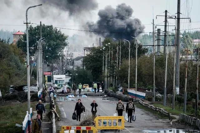 A woman (3rd R), evacuating with belongings, protects her ears after an explosion on a bridge over the Oskil River as black smoke rises in the frontline city of Kupiansk, Kharkiv region, on September 24, 2022, amid the Russian invasion of Ukraine. In the northeastern town of Kupiansk, which was recaptured by Ukrainian forces, clashes continued with the Russian army entrenched on the eastern side of the Oskil River. (Photo by Yasuyoshi Chiba/AFP Photo)