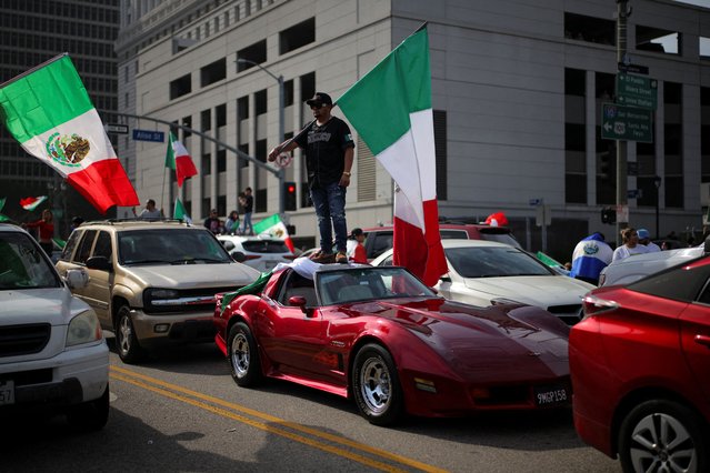 A man stands on a sports car with a flag during a protest against arrests and deportations of migrants by U.S. government agencies, in Los Angeles, California, on February 3, 2025. (Photo by Daniel Cole/Reuters)