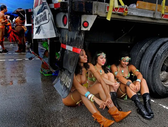 Miami Broward Carnival revelers from Coral Springs, Felisha Poulard, Nicole Marks, and Tiana Classen, find a dry spot underneath a sound truck during a downpour at Sun Life Stadium in Miami, on October 7, 2012. (Photo by Carl Juste/The Miami Herald)