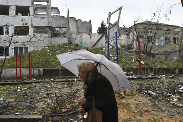 A woman walks past buildings damaged by Russian shelling in Druzhkivka, Donetsk region, Ukraine, Wednesday, October 26, 2022. (Photo by Andriy Andriyenko/AP Photo)
