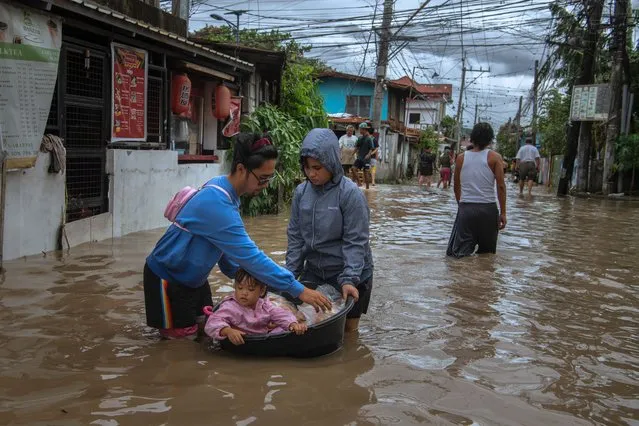 Residents wade through flood waters that barreled through their village on October 30, 2022 in Kawit, Philippines. Tropical Storn Nalgae made landfall in the Philippines on Saturday, leaving severe flooding, displacement, and destruction in its wake. Flash flooding and landslides have killed at least 47 with dozens still missing, local media reports said. (Photo by Jes Aznar/Getty Images)