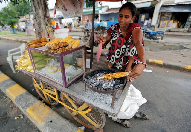 A woman roasts a corn to sell alongside a road in Ahmedabad, India August 30, 2016. (Photo by Amit Dave/Reuters)
