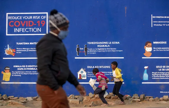 People walk past a COVID-19 advert promoting the use of face mask, washing of hands, use of sanitiser and social distance in the township of Soweto outside of Johannesburg, South Africa, Monday, July 13, 2020. South African President Cyril Ramaphosa said that top health officials warn of impending shortages of hospital beds and medical oxygen as South Africa reaches a peak of COVID-19 cases, expected between the end of July and September. South Africa's rapid increase in reported cases has made it one of the world's centers for COVID-19. (Photo by Themba Hadebe/AP Photo)