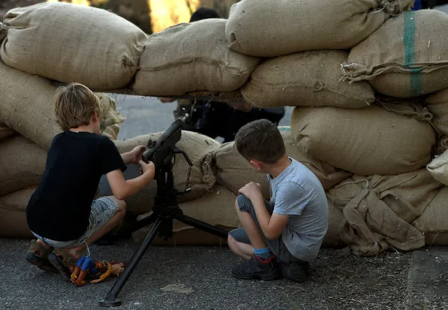 Two children play with a machine gun before members of the association historical recreation Frente del Nalon participate in the recreation of the battle: “The Siege of Oviedo” that took place during the Spanish Civil War, in Grullos, near Oviedo, in northern Spain, September 3, 2016. (Photo by Eloy Alonso/Reuters)