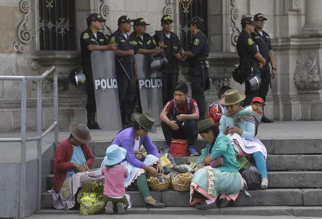 Women prepare to sell candy on the steps of the government palace where police stand guard and impeachment proceedings against Peru's President Pedro Pablo Kuczynski are going on in Lima, Peru, Wednesday, December 20, 2017. Congressional opposition leaders initiated the proceedings after an investigative committee revealed documents showing Kuczynski's private consulting firm received payments from Brazilian construction company Odebrecht more than a decade ago. (Photo by Martin Mejia/AP Photo)