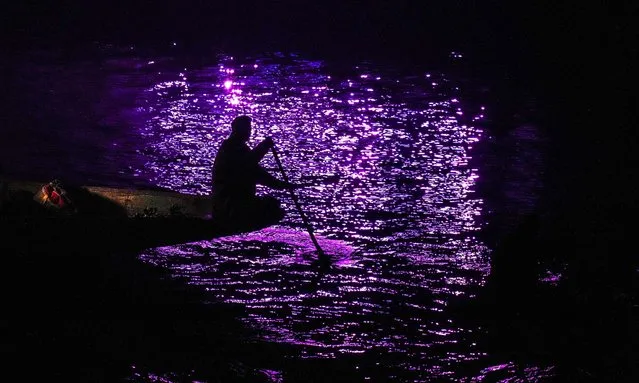 A Kashmiri boatman rows his boat as folk artists perform during a laser show and and live concert organized to boost winter tourism at the Dal Lake in Srinagar, Indian controlled Kashmir, Wednesday, December 7, 2022. (Photo by Mukhtar Khan/AP Photo)