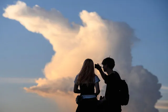 A couple take photos in front of a view of a cloud as the sun sets in Hong Kong on July 21, 2020. (Photo by Anthony Wallace/AFP Photo)