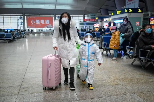 A woman leading child with personal protective equipment (PPE) walk at a railway station in Beijing on January 12, 2023, as the annual migration begins with people heading back to their hometowns for Lunar New Year celebrations. (Photo by Wang Zhao/AFP Photo)