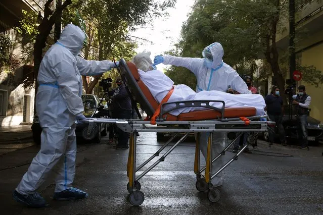 A paramedic with a special suit to protect against coronavirus, adjusts the face mask of a patient as his colleague pulls the stretcher out of a nursing home where dozens of elderly people have been found positive to COVID-19, in Athens, Thursday, October 1, 2020. Nationwide, Greece has been experiencing a resurgence of the virus, with the number of new daily cases often topping 300, and both deaths and the number of those in intensive care units rising. (Photo by Thanassis Stavrakis/AP Photo)