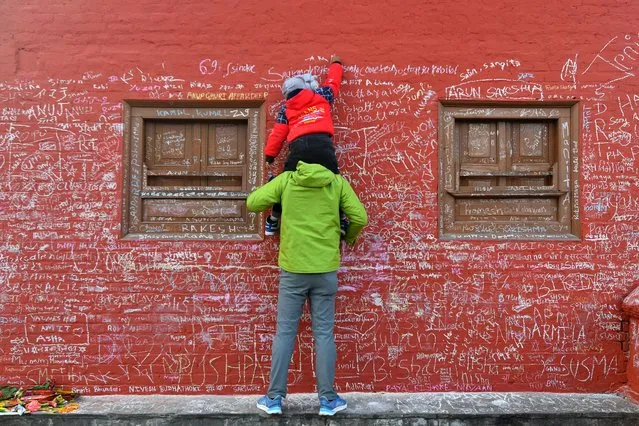 A child, helped by his father, writes a message with chalk on a wall at the Saraswati temple on the occasion of the Hindu festival of “Basanta Panchami”, in Kathmandu on January 26, 2023. (Photo by Prakash Mathema/AFP Photo)