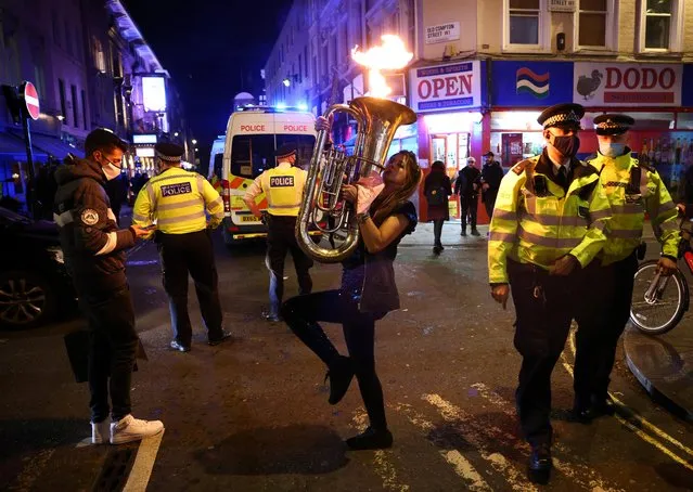A woman plays a musical instrument near police officers wearing protective face masks as pubs close ahead of the lockdown in Soho, London, Britain, November 4, 2020. (Photo by Henry Nicholls/Reuters)