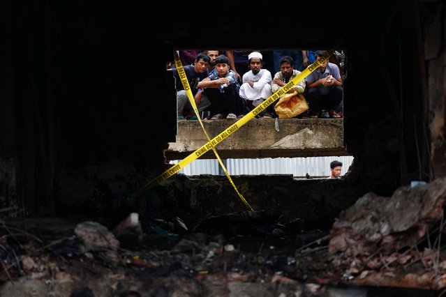 On lookers watch through a damaged window as members of Bangladesh Air Force work at the site, after an air force training aircraft crashed into a building belonging to Milestone School and College, in Dhaka, Bangladesh, on July 22, 2025. (Photo by Mohammad Ponir Hossain/Reuters)