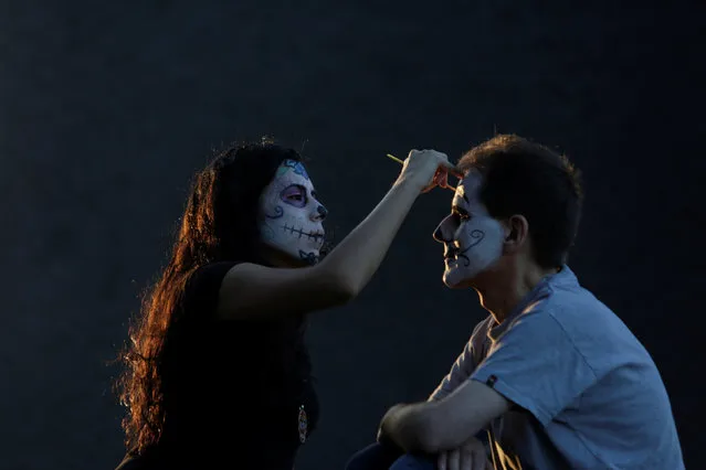 A woman with her face painted to look like the popular Mexican figure called “Catrina” paints the face of a man in Monterrey, Mexico October 30, 2016. (Photo by Daniel Becerril/Reuters)