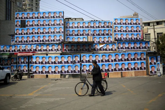 A man with a bicycle walks past a building covered in posters of Chinese President Xi Jinping in Shanghai, China, March 26, 2016. (Photo by Aly Song/Reuters)