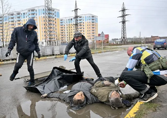 Communal workers collect the bodies of two men in the town of Bucha, not far from the Ukrainian capital of Kyiv on April 3, 2022. US and NATO leaders voiced shock and horror at new evidence of atrocities against civilians in Ukraine, and warned that Russian troop movements away from Kyiv did not signal a withdrawal or end to the violence. (Photo by Sergei Supinsky/AFP Photo)