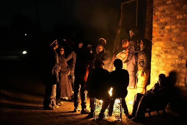 People huddle around a fire for warmth in the Angelo Informal Settlement in Boksburg, South Africa, on Thursday July 6, 2023. Police said a gas leak left multiple people dead including children. (Photo by Themba Hadebe/AP Photo)