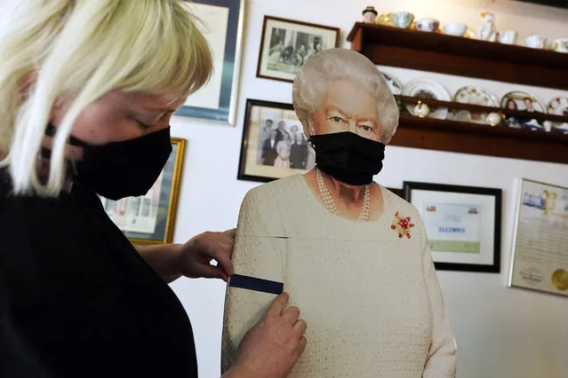 Molly Carew, manager of Tea & Sympathy, a British restaurant and shop, places a black arm band on a cardboard cutout of Queen Elizabeth II, to mourn the death of Britain's Prince Philip in New York, Friday, April 9, 2021. (Photo by Richard Drew/AP Photo)