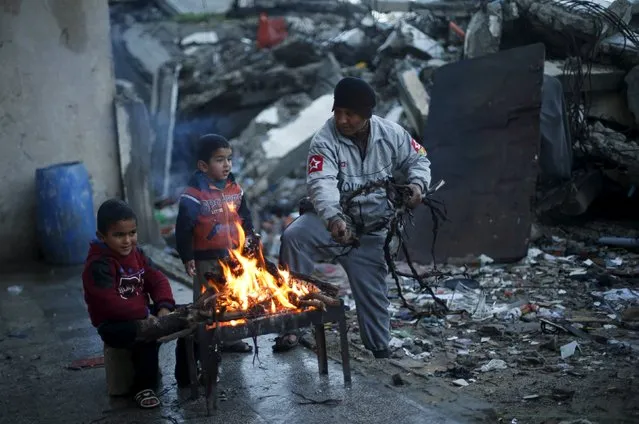 A Palestinian man uses tree branches to stoke a fire to warm himself and his grandsons near the ruins of a house destroyed during 2014 war, on a stormy day in Beit Hanoun in the northern Gaza Strip February 7, 2016. (Photo by Suhaib Salem/Reuters)