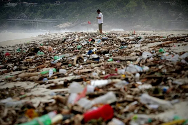 A man stands in garbage that was washed onto the beach of Sao Conrado following a storm in Rio de Janeiro, Brazil, 07 February 2019. At least five people died and others are missing due to the rain and storm that worsened during the night of 06 February in Rio de Janeiro. A “state of crisis” has been declared after the strong storm, official sources said 07 February. (Photo by Antonio Lacerda/EPA/EFE)