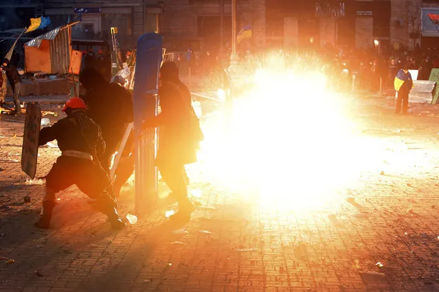 A stun grenade explodes as protesters clash with police during unrest in central Kiev, Ukraine, Monday, January 20, 2014. After a night of vicious streets battles, anti-government protesters and police clashed anew Monday. Hundreds of protesters, many wearing balaclavas, hurled rocks and stun grenades and police responded with tear gas. (Photo by Sergei Grits/AP Photo)