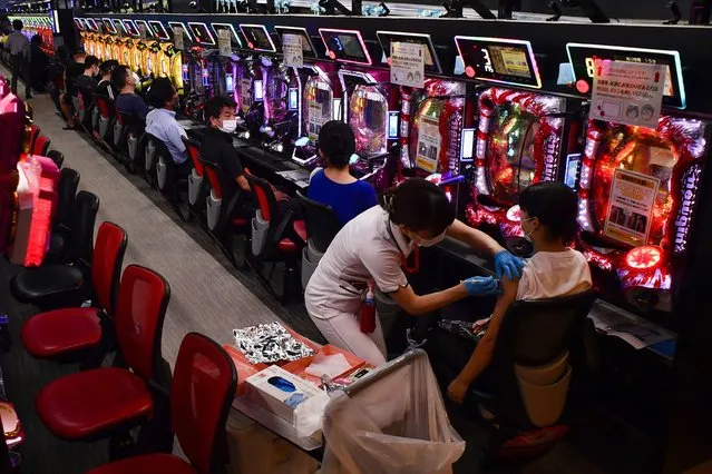 A woman receives the first shot of the Moderna COVID-19 vaccine as others wait for their turn in front of pachinko pinball machines at the pachinko parlor Freedom in Osaka, western Japan, Monday, September 13, 2021. A nearby hospital dispatched medical workers to administer the vaccine to 1,500 people in two days at the pinball parlor which became a makeshift vaccination site. (Photo by Kyodo News via AP Photo)