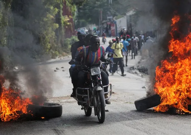 People on a motorcycle drive through a burning barricade set up in protest against the government and calling for the resignation of Prime Minister Ariel Henry, in Port-au-Prince, Haiti on February 5, 2024. (Photo by Ralph Tedy Erol/Reuters)