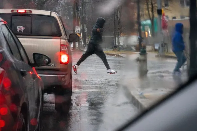 Takoma Park, Maryland - January 9:  A pedestrian leaps over a puddle at the intersection of Piney Branch Rd. And Flower Ave. in Takoma Park, MD. On Tuesday, January 9, 2024, Governor Moore declared a State of Preparedness in Maryland due to flooding rains, coastal flooding, strong winds, and mountain wintry precipitation. Some school districts, such as Montgomery County dismissed early. (Photo by Sarah L. Voisin/The Washington Post)