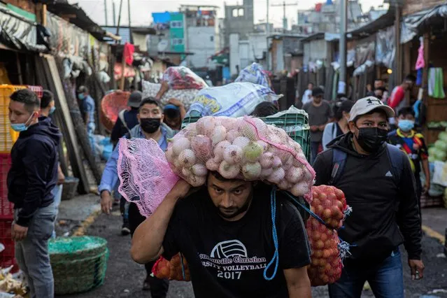A man carries a bag of onions through a crowded street that is part of La Terminal Market after the government implemented new restrictions to contain the spread of COVID-19 Delta variant, including a nighttime curfew, in Guatemala City, Monday, August 16, 2021. (Photo by Oliver de Ros/AP Photo)