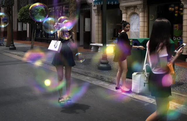 A tourist takes pictures amidst soap bubbles from a mist blowing machine at Universal Studios, a popular tourist destination, Wednesday, April 8, 2015, in Sentosa, Singapore. (Photo by Wong Maye-E/AP Photo)