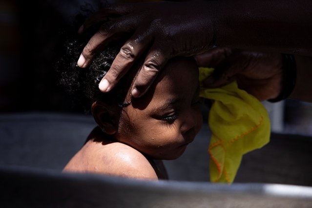 A woman bathes a baby displaced by gang war violence at the Antenor Firmin high school transformed into a shelter where people live in poor conditions, in Port-au-Prince, Haiti on May 1, 2024. (Photo by Ricardo Arduengo/Reuters)