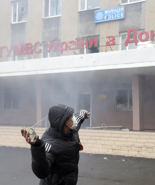 A pro-Russian man throws a stone during the mass storming of a police station in the eastern Ukrainian town of Horlivka on Monday, April 14, 2014. Text on the building reads: “Horlivka's police”.  Several government buildings has fallen to mobs of Moscow loyalists in recent days as unrest spreads across the east of the country. (Photo by Efrem Lukatsky/AP Photo)