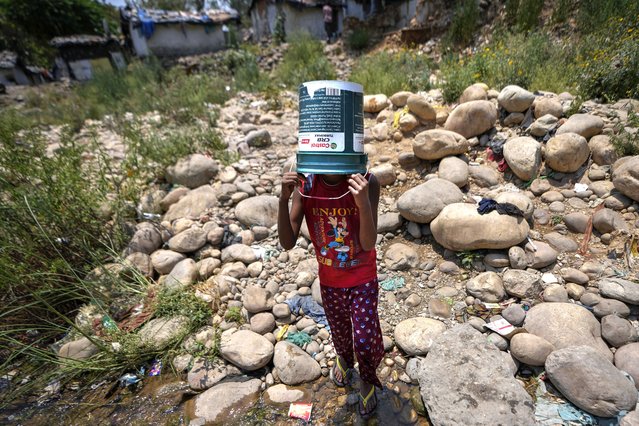 A girl covers her head with a repurposed engine oil container to shield herself from the sun as she walks to collect water from a leaking municipal pipe on a hot summer day on the outskirts of Jammu, India, Friday, May 31, 2024. Officials say a scorching heat wave has killed at least 14 people, including 10 election officials, in eastern India with temperatures soaring up to 49.9 degrees Celsius (122 degrees Fahrenheit) in parts of India this week. (Photo by Channi Anand/AP Photo)