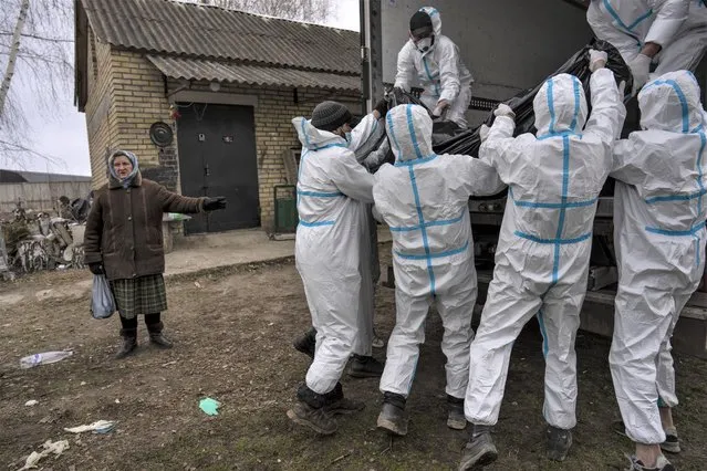 Nadiya Trubchaninova, 70, left, stands next to volunteers while loading a plastic bag that contains the body of a civilian killed by Russian soldiers into a truck, in Bucha, in the outskirts of Kyiv, Ukraine, Tuesday, April 12, 2022. (Photo by Rodrigo Abd/AP Photo)