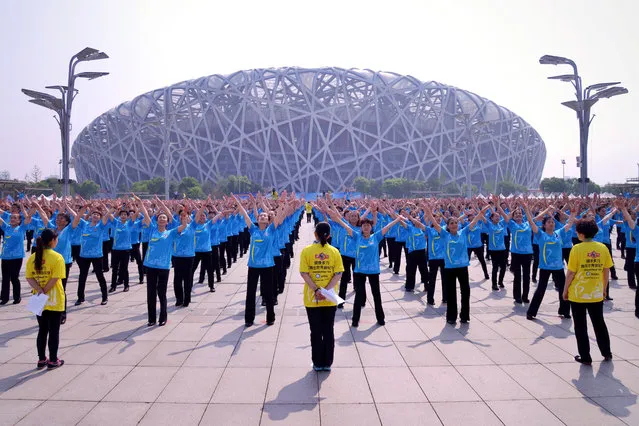 In this Saturday, May 21, 2016 photo, people dance in unison outside of the National Stadium, also known as the Bird's Nest, in Beijing. According to the Guinness World Records website, 31,697 participants in Beijing, Shanghai and four other cities set a new world record on Saturday for mass plaza dancing in multiple locations by performing choreographed dance moves together for more than five minutes. (Photo by Chinatopix via AP Photo)