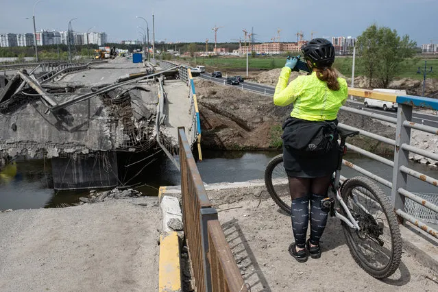 A cyclist photographs the destroyed bridge over the Irpin river on May 7, 2022 in Irpin, Ukraine. Following Russia's retreat from areas around the Ukrainian capital, signs of normal life have returned to Kyiv, with residents taking advantage of shortened curfew hours, businesses reopening, and foreign countries promising to return their diplomats. (Photo by Alexey Furman/Getty Images)