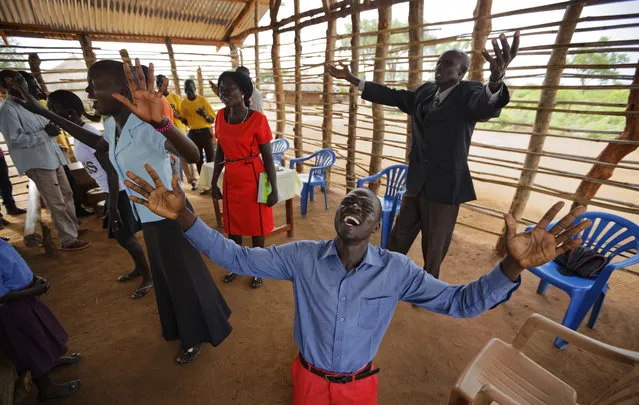 In this photo taken Sunday, June 4, 2017, preacher Daniel Rasash falls to his knees and weeps in prayer, at the Yoyo Pentecostal Church in Bidi Bidi refugee settlement in northern Uganda. The South Sudanese refugees meet in open-air churches rigged from timber with seats made only from planks of wood or logs drilled into the ground, yet these churches for the born-again Christians are oases of joy among the daily humiliations that come with rebuilding their lives. (Photo by Ben Curtis/AP Photo)