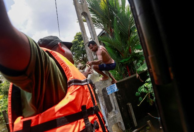 A flood victim hangs on a light post to receive lunch packets for his family on a flooded road from Sri Lankan army members in Kelaniya, Sri Lanka on June 4, 2024. (Photo by Dinuka Liyanawatte/Reuters)