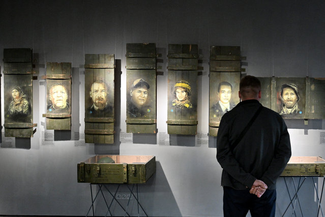 A man stands next to portraits of deceased Ukrainian soldiers painted on parts of shell boxes by French street artist Christian Guemy (aka C215) during the opening of his exhibition “Guerre en Ukraine” (War in Ukraine) in the Exhibition Center of the War Museum in Kyiv on July 8, 2023. The exhibition presented the artist works which he created  in Ukraine for 18 monthes and including video, installation, war items, portraits of Ukrainian fallen heroes, personal objects belonging to them, and a tribute portrait of AFP journalist Arman Soldin fallen near Bakhmut this year. (Photo by Sergei Supinsky/AFP Photo)