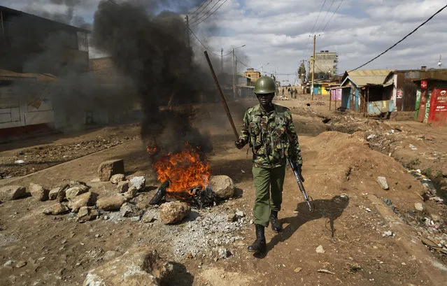 A riot policeman walks past burning barricades erected by protesters throwing rocks, during clashes in the Kawangware slum of Nairobi, Kenya Thursday, August 10, 2017. International observers on Thursday urged Kenyans to be patient as they awaited final election results following opposition allegations of vote-rigging, but clashes between police and protesters again erupted in Nairobi. (Photo by Ben Curtis/AP Photo)
